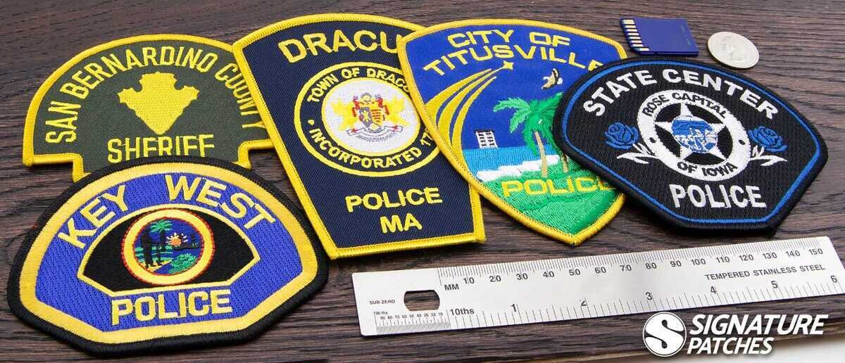 Collection of custom police patches including San Bernardino County Sheriff, Key West Police, Dracut MA, Titusville, and State Center Iowa