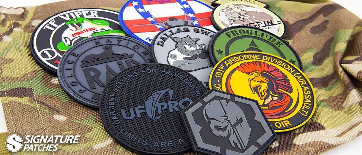Collection of custom PVC morale patches displayed on camouflage fabric, featuring military and law enforcement designs